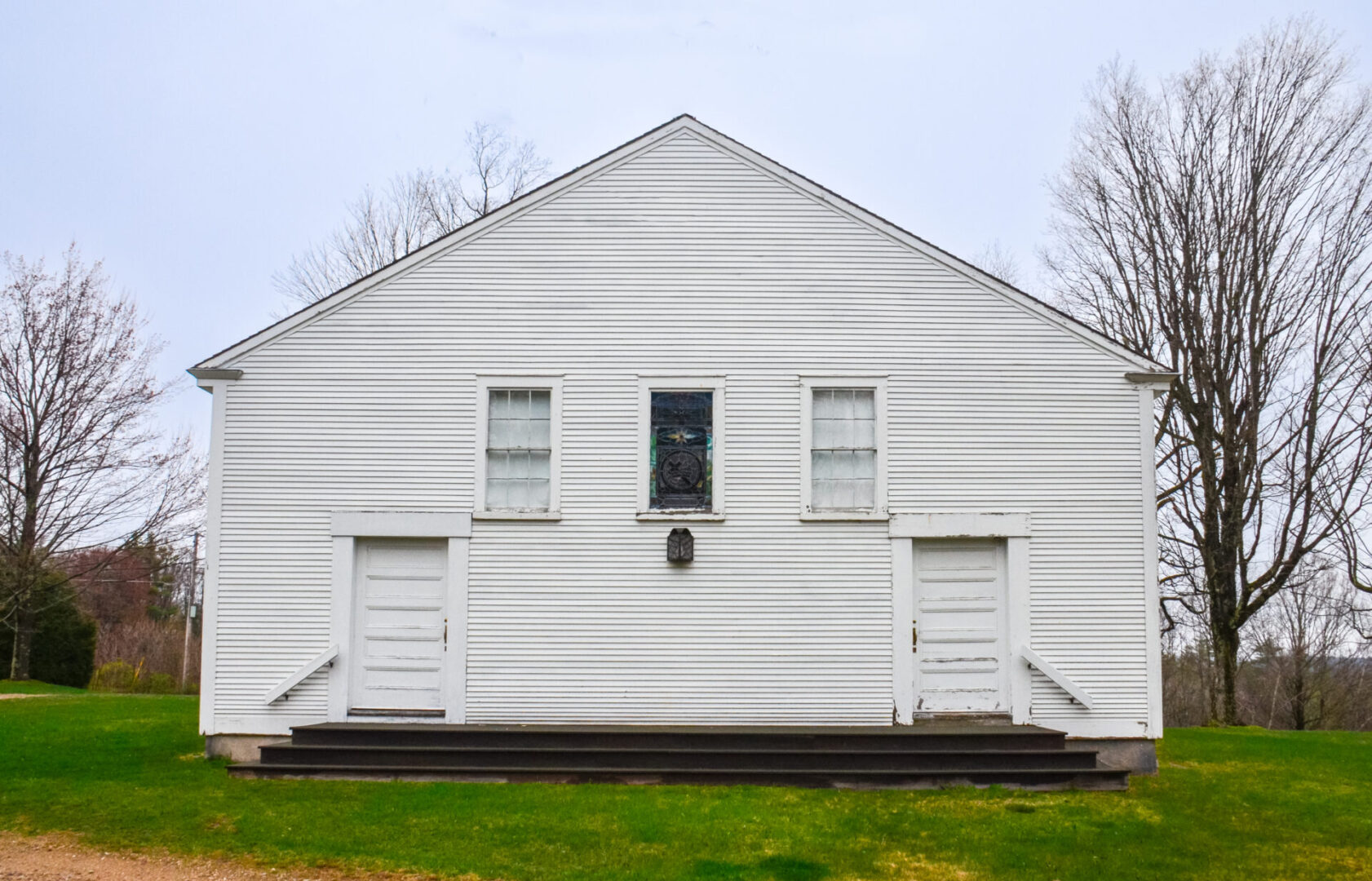 A white building with two windows and steps leading to it.